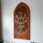 Decorative wooden wall panel with intricate carvings on a white wall.